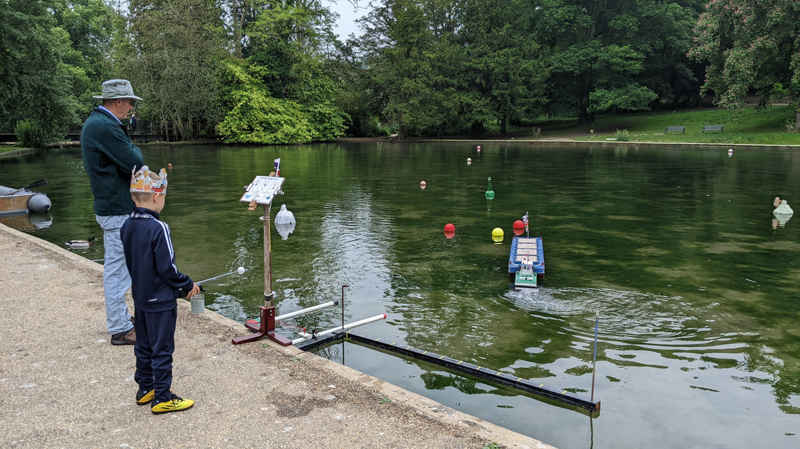 Under supervision, a photo of a child operating a radio controlled boat on the lake.