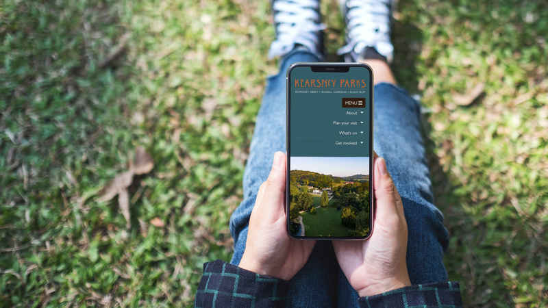 A photograph of a person sat viewing the Kearsney Parks website on a smartphone.